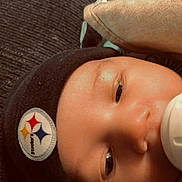 Colt is registered to the contest to win money with this photo: baby, face, beanie, bottle, blanket, close_up, child, infant, soft_lighting, cozy, sleepy, black_clothing, logo, indoor, portrait, cute, headwear, young_child, feeding, resting
