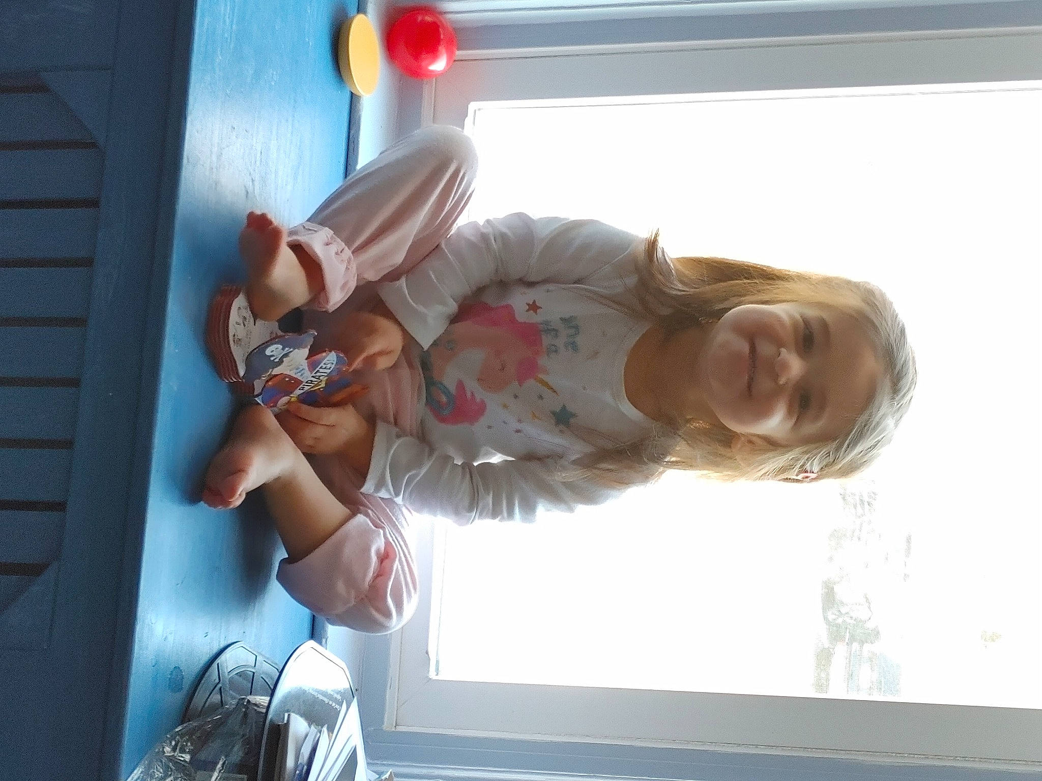 Riley is registered to the contest to win money with this photo: bag, child, eyewear, finger, fun, gesture, happy, human_leg, joy, luggage_and_bags, person, room, sitting, smile, toddler, tree, window