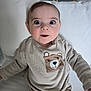 Ernest a rejoint le concours — aidez-le/la à gagner de superbes lots ! baby, child, infant, wide_eyes, surprised_expression, beige_sweater, bear_patch, cushion, rattan_chair, white_background, seated, indoors, cute, portrait, cozy, soft_lighting, casual_clothing, young, smiling, person