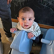 Ernest a rejoint le concours — aidez-le/la à gagner de superbes lots ! baby, child, toy, scooter, blue, indoor, floor, chalkboard, chalk, hand, person, legs, curious, playful, expression, clothing, wooden_floor, wheels, furniture, young