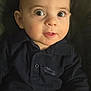 baby, child, face, eyes, curious, portrait, infant, clothing, dark_shirt, car_emblem, closeup, cute, person, skin, expression, indoors, young, head, sitting, soft_lighting