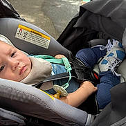 Howard joined the competition — help win amazing prizes! baby, infant, child, car_seat, vehicle, harness, pacifier, sitting, lying_down, face, portrait, eyes, cozy, clothing, socks, blue, gray, indoor, travel,  안전