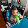 Marcus Nay is registered to the contest to win money with this photo: baby, child, high_chair, sippy_cup, drinking, indoors, kitchen, dining_area, table, chair, toy, teddy_bear, appliances, clothing, short_sleeves, portrait, sitting, focused, home, wooden_floor