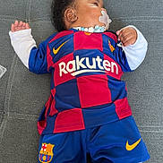Kaydenn a rejoint le concours — aidez-le/la à gagner de superbes lots ! child, baby, pacifier, pacifier_clip, fc_barcelona_jersey, rakuten_logo, nike_swoosh, sports_shorts, knee_socks, curly_hair, couch, grey_upholstery, teal_blanket, baby_bottle, lying_down, indoor, portrait, infant_clothing, hand, cute