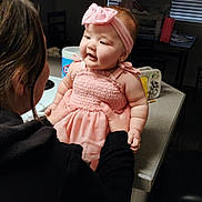 Journey is registered to the contest to win money with this photo: adult_hand, arm, baby, chair, child, counter, cute, earrings, face, happy, headband, indoor, kitchen, light, person, pink_dress, skin, smile, table, window_blinds