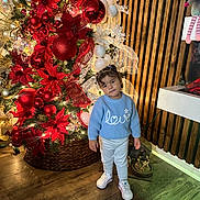 Grace joined the competition — help win amazing prizes! toddler, child, blue_sweater, love, christmas_tree, red_poinsettias, ornaments, holiday_decor, indoor, wooden_floor, wooden_wall, festive, cute, smiling, white_pants, white_sneakers, lighting, portrait, holiday, seasonal