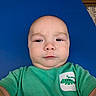 baby, child, selfie, green_shirt, lizard_graphic, blue_mat, closeup, face, expression, casual_clothing, indoors, portrait, young_child, cute, serious_face, skin, head, person, infant, toddler