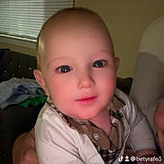 Axel Gael is registered to the contest to win money with this photo: baby, child, clothing, couch, expression, eyes, face, hand, holding, human, indoor, person, plaid, portrait, shirt, skin, social_media, toddler, window_blinds, young