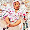 baby, child, smiling, floral_robe, headband, makeup_brush, cosmetics, lipstick, eyelash_curler, false_eyelashes, nail_polish, face_cream, brush, bed_sheet, pink, white, cute, happy, lying_down, portrait