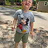 child, boy, cap, tshirt, mickey_mouse, shorts, green_shoes, outdoor, daylight, road, trees, sunlight, shadow, playful, cute, casual_clothing, smiling, standing, nature, summer