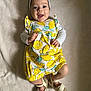 baby, infant, smiling, headband, flower, lemon_pattern, romper, white_sandals, lying_down, blanket, happy, cute, child, clothing, footwear, portrait, indoors, person, baby_fashion, soft_texture