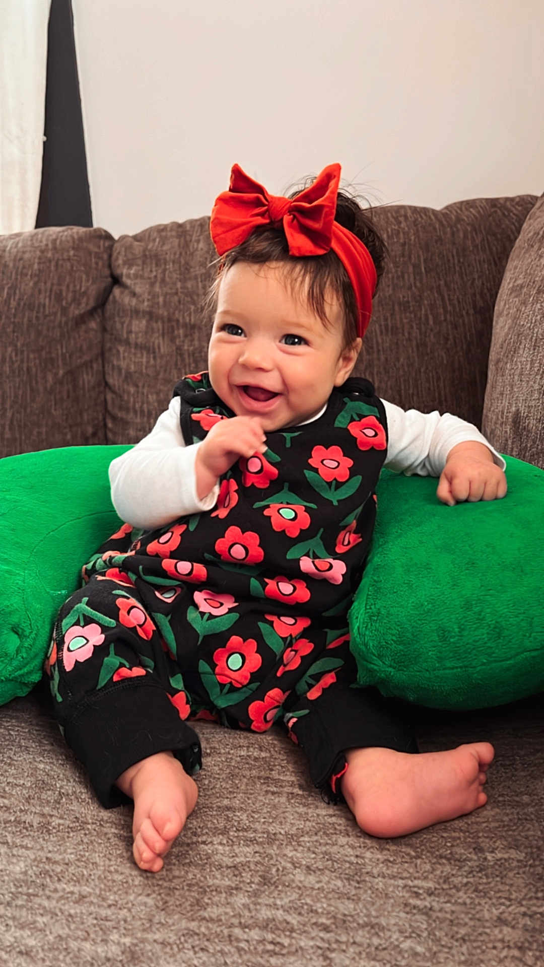 Bellamy is registered to the contest to win money with this photo: baby, child, smiling, couch, green_cushion, red_bow, floral_outfit, happy, indoors, sitting, barefoot, cute, headband, infant, portrait, comfortable, cozy, person, home, bright
