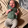 baby, child, infant, smiling, laughing, portrait, lying_down, bed, blanket, hooded_clothing, green_outfit, gray_pants, bare_feet, hands, face, indoor, bedroom, cozy, happy, photography