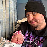 Auggie is registered to the contest to win money with this photo: adult, baby, beanie, blanket, boy, clothing, curtain, face, facial_hair, hat, indoor, man, newborn, person, portrait, sleeping, towel, wearing, window, young_child