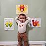 Marcus May Jr is registered to the contest to win money with this photo: toddler, child, standing, foam_mat, thanksgiving, wall_art, drawing, corn, turkey, clothing, long_sleeve, pants, barefoot, indoor, home, smiling, cute, pose, colorful, floor