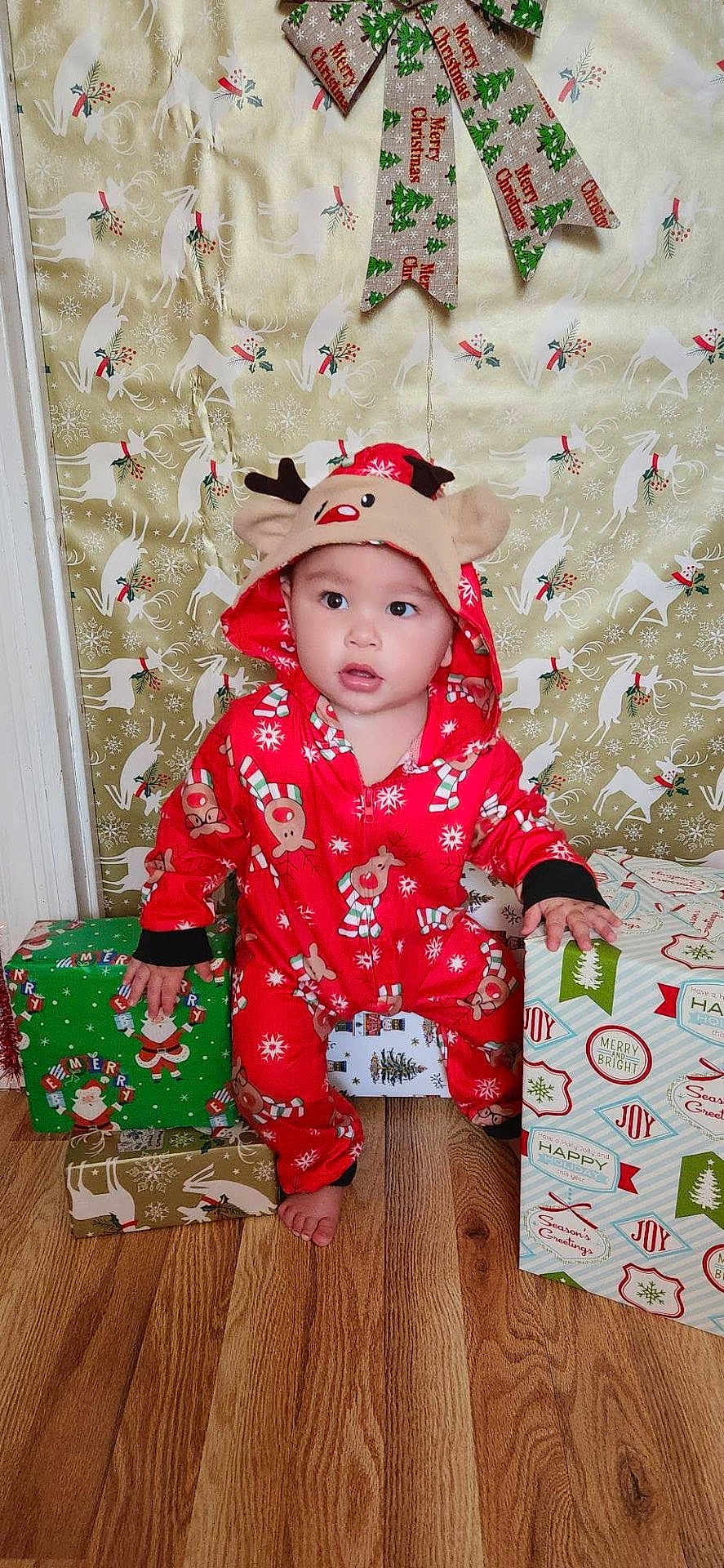 Marcus May Jr is registered to the contest to win money with this photo: toddler, child, christmas, holiday, presents, gift_wrap, reindeer, onesie, red_clothing, floor, wood_floor, indoor, festive, background, curious, barefoot, holiday_decor, face, person, seasonal