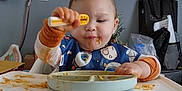 Marcus May Jr is registered to the contest to win money with this photo: toddler, high_chair, spaghetti, messy, child, eating, pajamas, pumpkin, food, plate, utensil, bib, indoor, kitchen, cabinet, plastic_bag, face, hand, tray, seat
