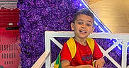 Jacob is registered to the contest to win money with this photo: backpack, bench, boy, casual_wear, child, colorful, floor, happy, heart_shape, indoor, neon_light, people, portrait, purple_flowers, red_clothing, retail, shoes, shopping_mall, smiling, store