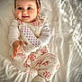 baby, child, infant, pink, headband, shoes, flower_pattern, pajamas, smiling, happy, cute, bed, white_bedspread, playful, portrait, indoors, soft_lighting, clothing, person, lying_down