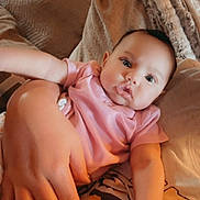 Isla joined the competition — help win amazing prizes! baby, infant, pink_shirt, hand, adult_hand, nail_polish, blanket, couch, cozy, soft, comfort, child, portrait, face, skin, furniture, relaxing, indoors, warm_lighting, person