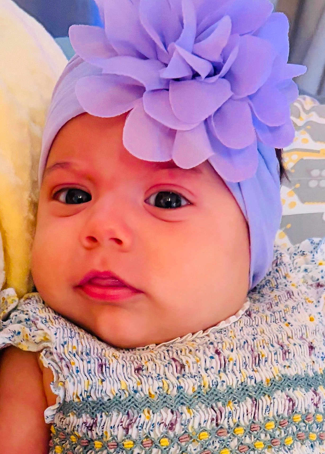 Julia is registered to the contest to win money with this photo: baby, infant, headband, flower, purple, face, eyes, clothing, patterned, blanket, pillow, closeup, skin, cute, young, child, portrait, resting, soft, indoors