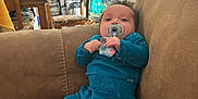 Niklaus is registered to the contest to win money with this photo: baby, pacifier, couch, blue_outfit, infant, socks, living_room, curtain, dining_table, chair, candy_box, fish_tank, lamp, doorway, home_interior, cushion, plush_toy, household_items, portrait, relaxed