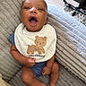 Kyrie Parker is registered to the contest to win money with this photo: baby, infant, bib, bear, smile, mouth_open, couch, fabric, texture, blue_clothing, cute, happy, child, sitting, indoors, skin, foot, hand, plush, comfort