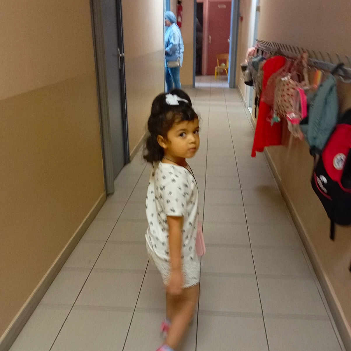 Cilia Soltan a rejoint le concours — aidez-le/la à gagner de superbes lots ! backpacks, bag, casual_clothing, child, curious, doorway, footwear, girl, hair_bow, hallway, indoor, looking_back, person, pink_shoes, school, shorts, tile_floor, walking, white_shirt, woman
