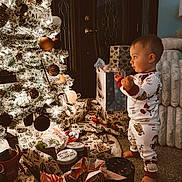 Bodhi joined the competition — help win amazing prizes! carpet, celebration, child, christmas_tree, cute, decorations, door, excitement, festive, furniture, gift_bags, holiday, indoors, lights, ornaments, pajamas, pine_cones, presents, toddler, wrapped_gifts