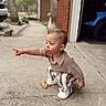 toddler, child, pointing, curious, outdoor, driveway, garage, car, clothing, striped_pants, knitted_top, squatting, side_profile, concrete, person, young_child, casual, daylight, expression, curiosity