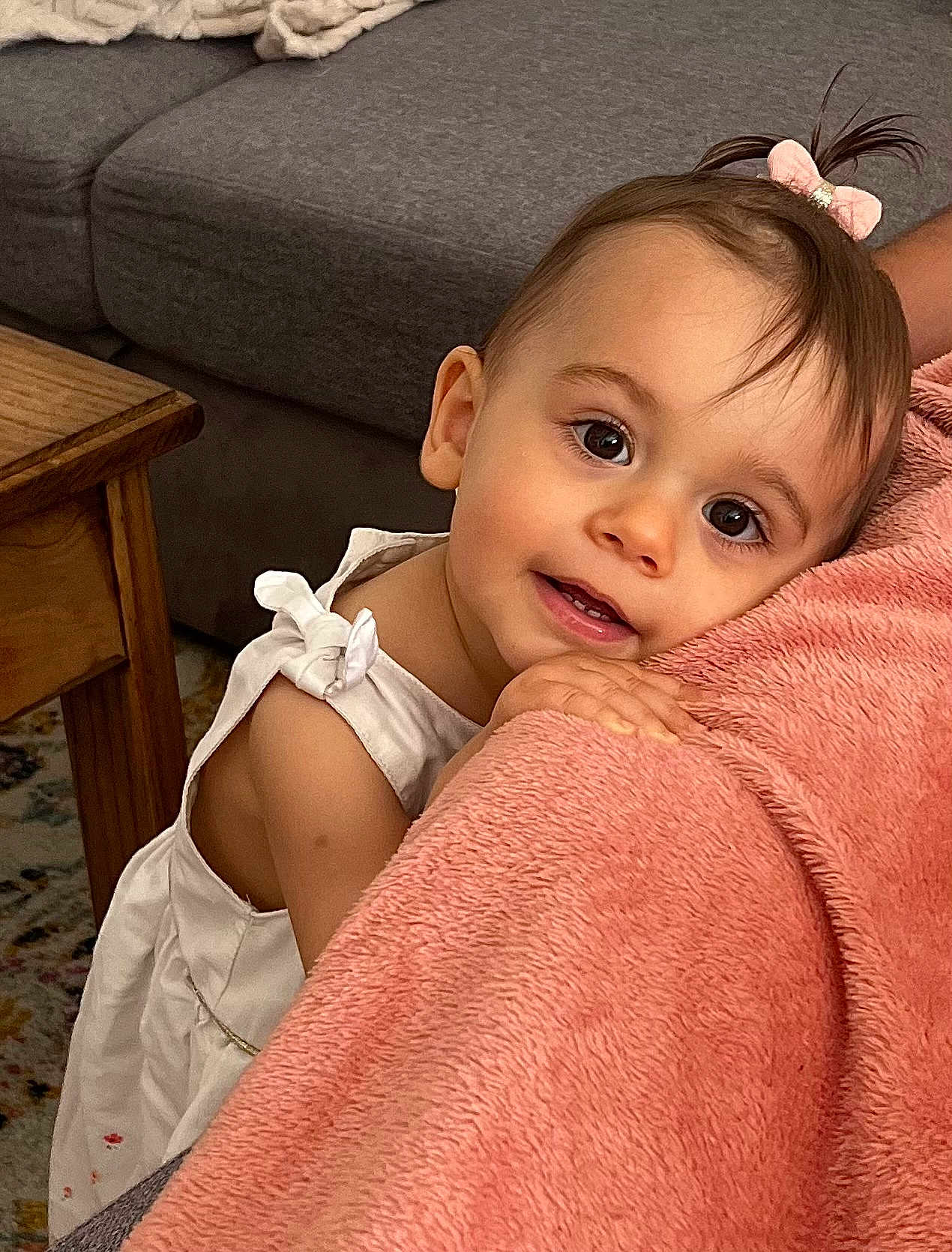 Octavia participe au concours pour gagner de l'argent avec cette photo : toddler, child, baby, girl, pink_bow, white_dress, blanket, couch, wooden_table, carpet, indoor, portrait, cute, smiling, curly_hair, hand, face, eyes, skin, cozy
