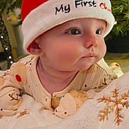 Logan joined the competition — help win amazing prizes! baby, infant, santa_hat, christmas, holiday, pajamas, blanket, snowflake, decorations, christmas_tree, festive, cute, child, face, indoors, cozy, soft_texture, red_hat, sleepwear, holiday_season