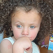 Maeva participe au concours pour gagner de l'argent avec cette photo : child, curly_hair, blue_eyes, white_top, indoor, thoughtful, hand_on_mouth, pink_hair_clip, knitted_clothing, young, portrait, cute, person, face, skin, expression, hair, table, background, natural_light