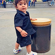 Advik is registered to the contest to win money with this photo: background, bench, black_clothing, casual, child, city, curly_hair, daytime, fountain, historic_buildings, outdoor, people, playful, shorts, sidewalk, sneakers, street, toddler, tourist_spot, urban