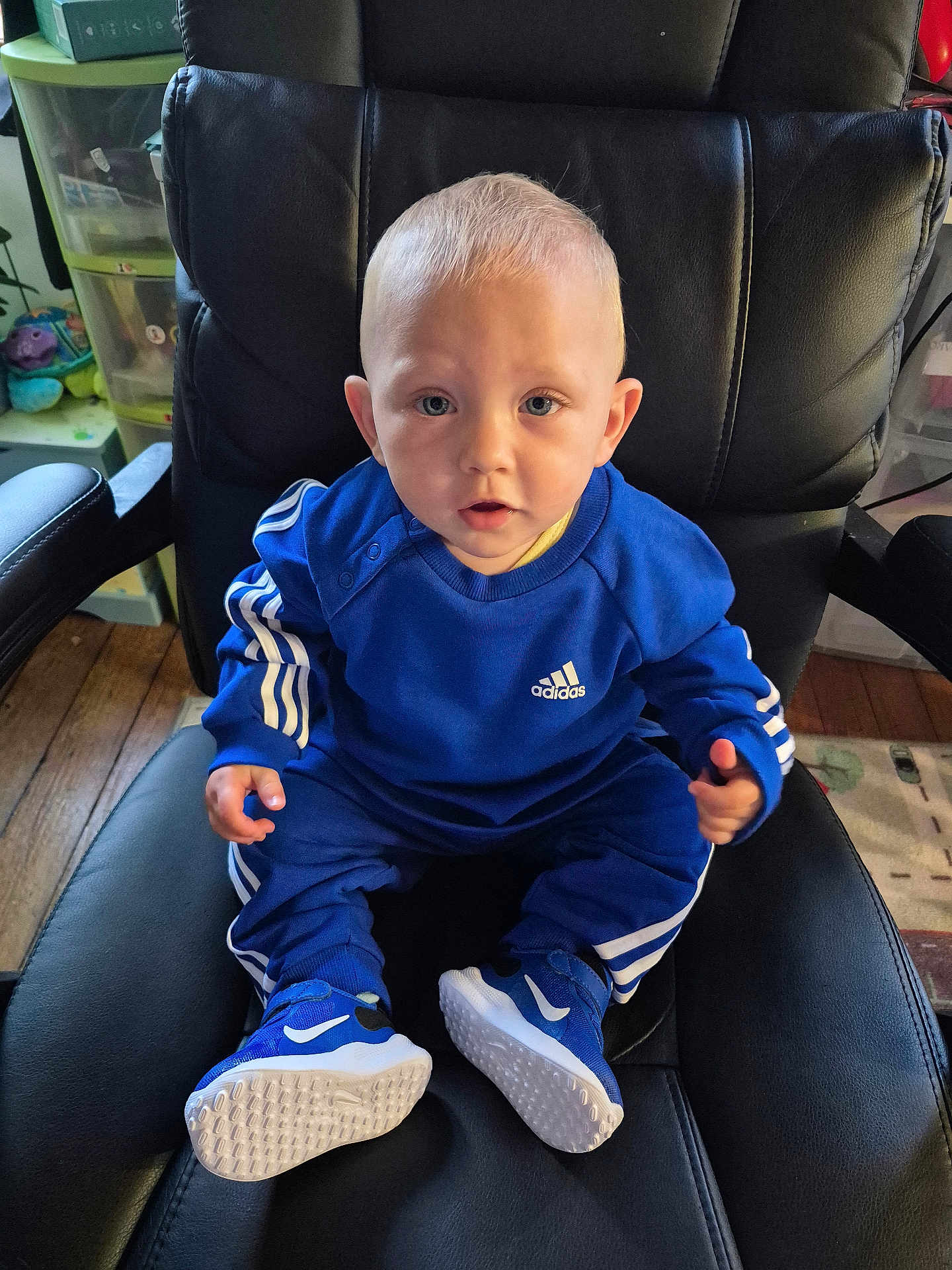Léon participe au concours pour gagner de l'argent avec cette photo : toddler, child, blue_clothing, adidas, sneakers, nike, sitting, chair, leather_chair, indoor, wooden_floor, toy, storage, curious, person, portrait, baby, face, shoes, casual