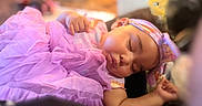 Phorever is registered to the contest to win money with this photo: arm, baby, blanket, child, closed_eyes, cozy, face, hand, headband, home, indoors, infant, nap, peaceful, portrait, purple_dress, resting, ruffles, sleeping, soft_lighting