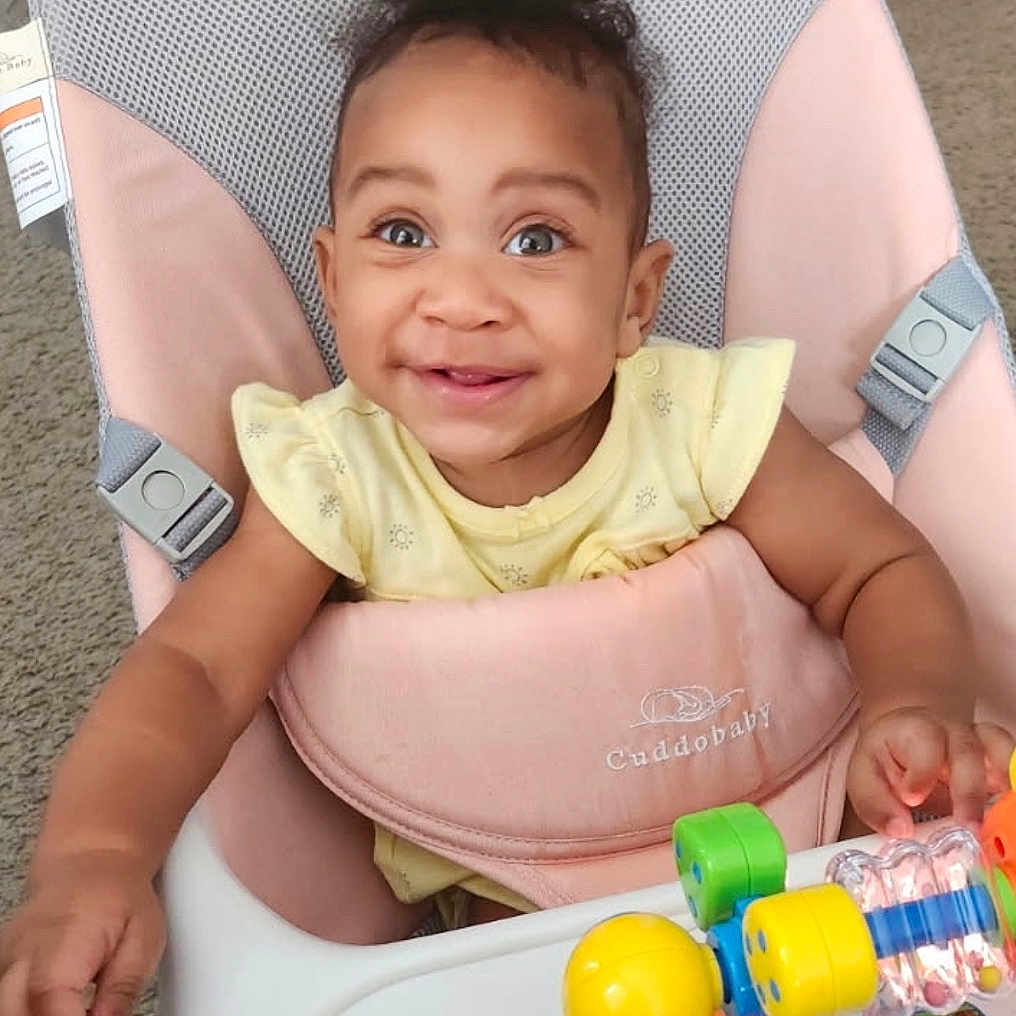 Kalii is registered to the contest to win money with this photo: baby, baby_chair, bright_eyes, carpet, child, clothing, colorful, curly_hair, face, furniture, hand, happy, indoor, person, playtime, seat, smiling, toddler, toy, young_child