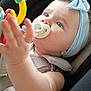 baby, pacifier, headband, blue_eyes, car_seat, toy, hand, harness, warning_label, clothing, child, infant, seatbelt, closeup, indoor, cute, expression, person, accessory, safety