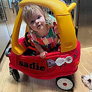 Sadie Jaymes joined the competition — help win amazing prizes! toddler, child, toy_car, red, yellow, indoor, kitchen, wood_floor, dog, pet, curious, colorful_clothing, window, appliances, flooring, playtime, plastic, person, face, vehicle