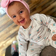ïwen participe au concours pour gagner de l'argent avec cette photo : baby, child, smiling, pink_bow, headband, pajamas, strawberry_pattern, sitting, happy, indoors, face, cute, infant, clothing, person, portrait, closeup, soft_texture, wood_floor, playful