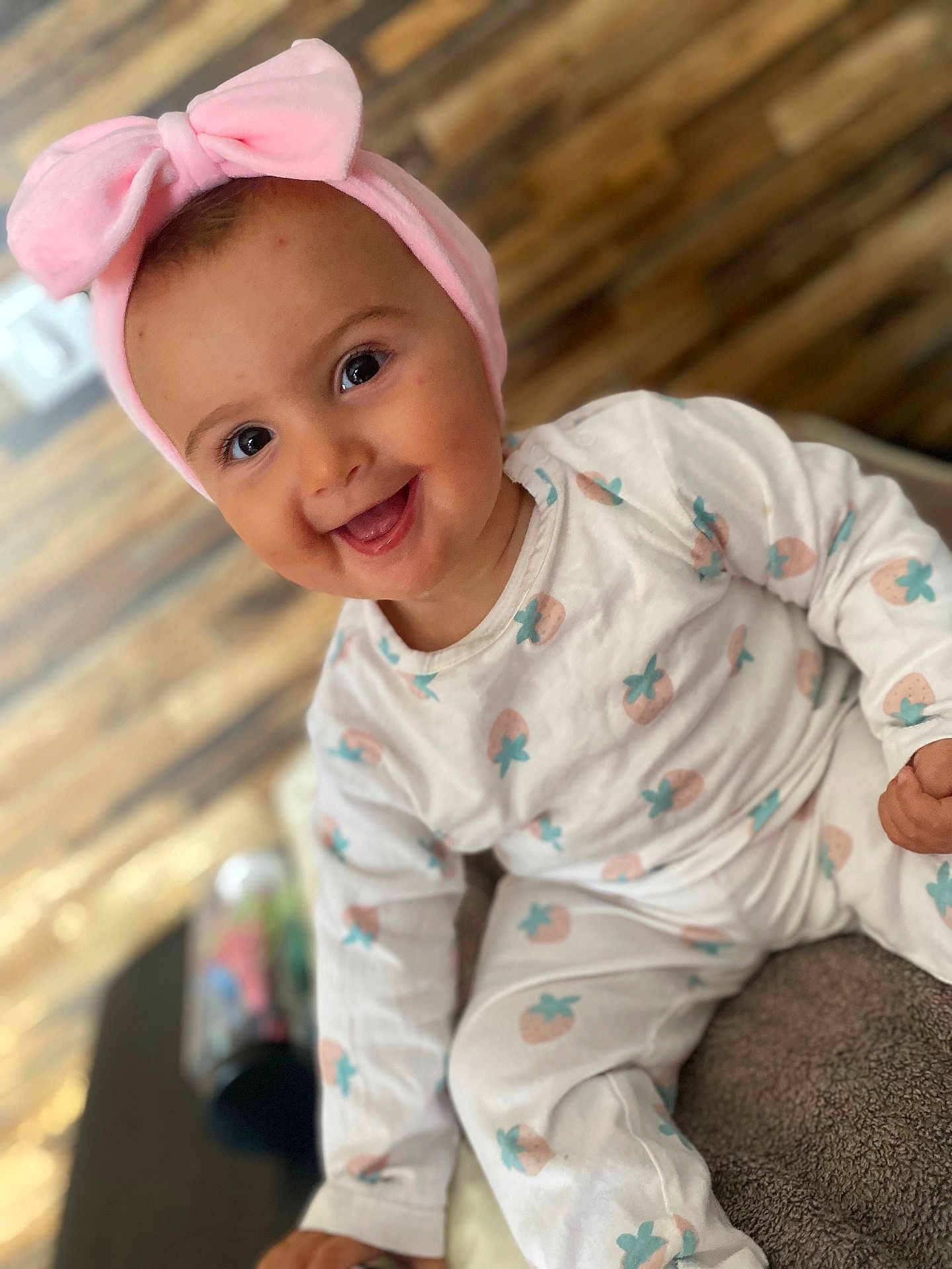 ïwen participe au concours pour gagner de l'argent avec cette photo : baby, child, smiling, pink_bow, headband, pajamas, strawberry_pattern, sitting, happy, indoors, face, cute, infant, clothing, person, portrait, closeup, soft_texture, wood_floor, playful