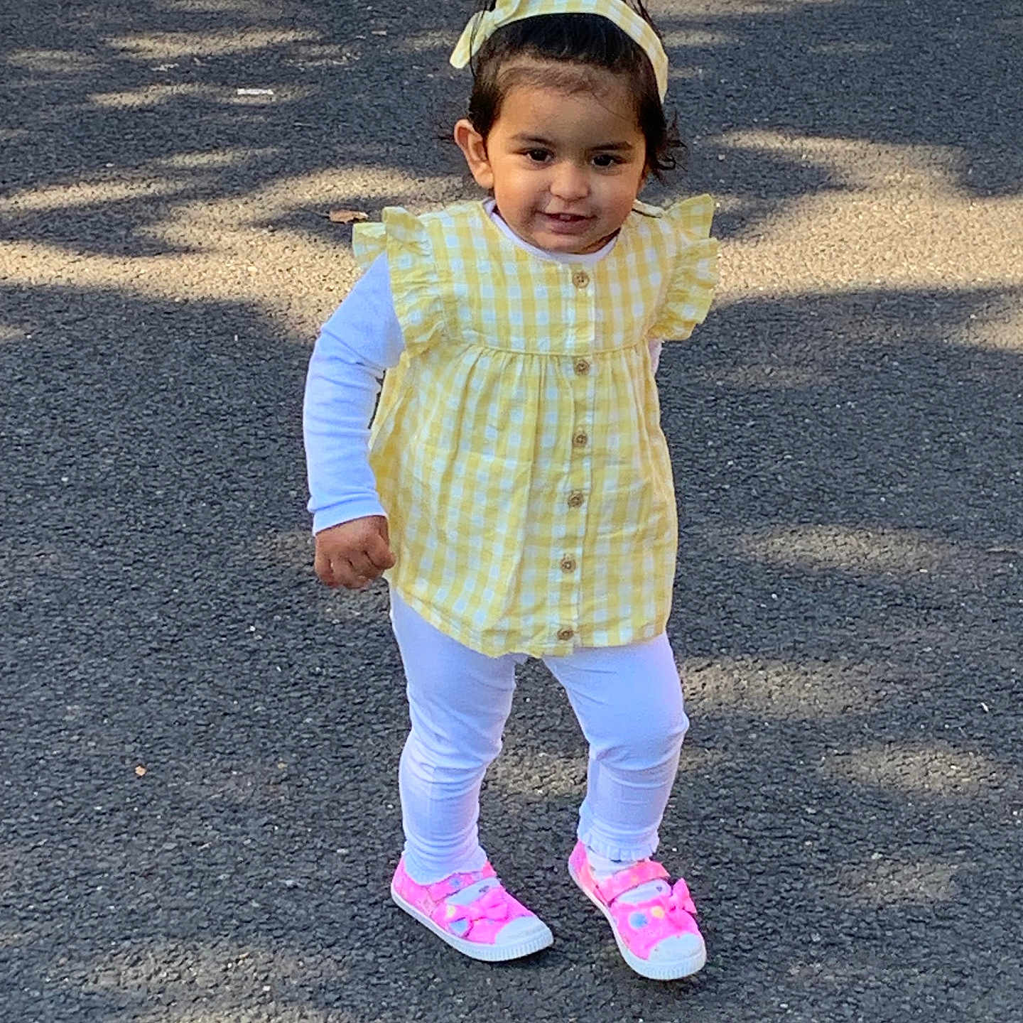Anokhi is registered to the contest to win money with this photo: casual_clothing, child, cute, daytime, fashion, happy, headband, outdoor, pavement, person, pink_shoes, playful, shadow, smiling, sunlight, toddler, walking, white_leggings, yellow_checkered, young_child