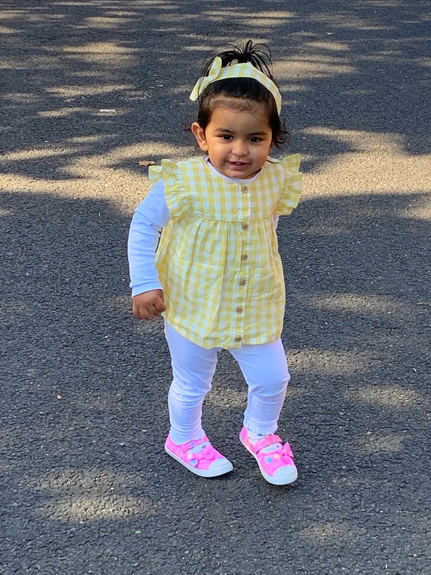 Anokhi is registered to the contest to win money with this photo: toddler, child, yellow_checkered, headband, pink_shoes, white_leggings, outdoor, pavement, sunlight, shadow, cute, walking, happy, person, young_child, casual_clothing, daytime, smiling, fashion, playful
