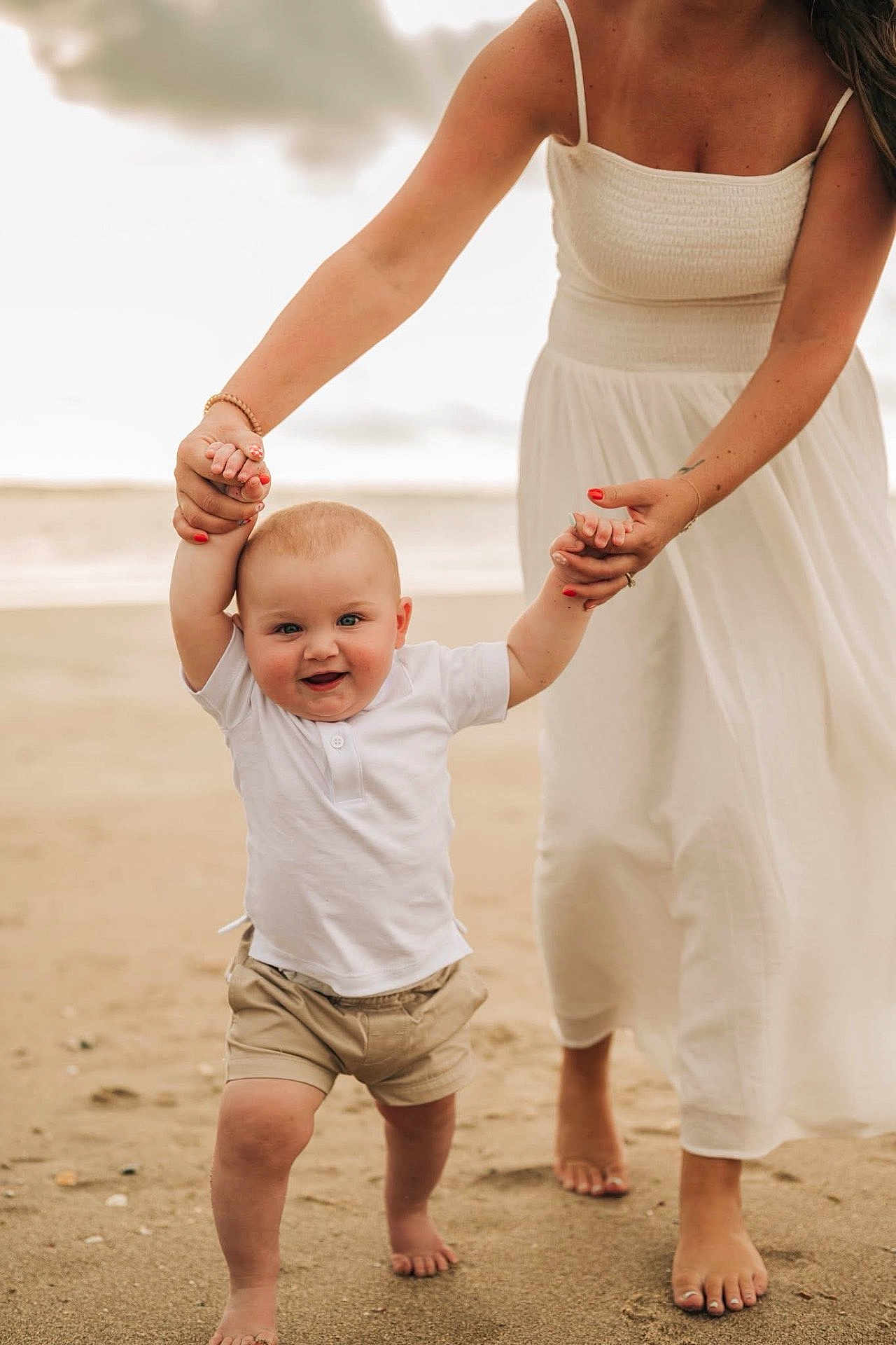 Tate joined the competition — help win amazing prizes! baby, child, beach, sand, walking, adult, hand_holding, white_shirt, shorts, barefoot, smiling, outdoor, summer, parent, woman, dress, happy, first_steps, support, nature