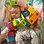 animal_print, baby, baby_seat, child, colorful, colorful_toys, cute, expression, face, floor, floral_onesie, indoor, infant, patterned_clothing, playtime, sitting, small_child, toy, wooden_blocks, wooden_floor