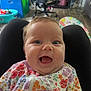 Lucia is registered to the contest to win money with this photo: baby, blurred_background, chair, child, clothing, comfort, expression, eyes, face, floor, floral_pattern, happy, head, home, indoors, mouth, onesie, person, skin, smiling