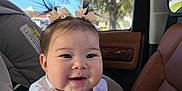 Scotti is registered to the contest to win money with this photo: baby, infant, smiling, pigtails, hair_bows, car_seat, car_interior, window, tree, sunlight, chubby_cheeks, portrait, cute, seatbelt, mirror_reflection, door_panel, tshirt, happy, foot, skin