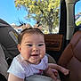 baby, infant, smiling, pigtails, hair_bows, car_seat, car_interior, window, tree, sunlight, chubby_cheeks, portrait, cute, seatbelt, mirror_reflection, door_panel, tshirt, happy, foot, skin
