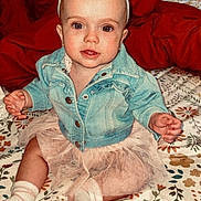 Kambri is registered to the contest to win money with this photo: baby, child, denim_jacket, headband, bow, tutu, socks, bedspread, floral_pattern, indoor, portrait, cute, smiling, seated, infant, cozy, pillow, wall, wood, brick