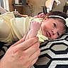 Gia is registered to the contest to win money with this photo: baby, newborn, infant, yellow_clothing, headband, flower, hand, cushion, pattern, geometric_pattern, indoor, resting, portrait, person, soft_lighting, closeup, skin, human, tender, cute
